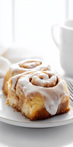 two cinnamon rolls on a white plate with a cup of coffee in the back ground