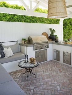 an outdoor kitchen with grill, sink and table on brick flooring next to white walls