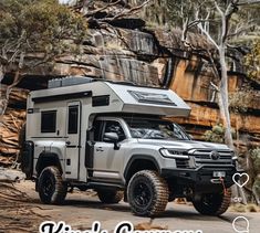 a truck with a camper attached to it parked in front of some rocks and trees