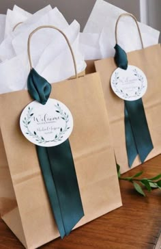 two brown paper bags with green ribbons and tags on them sitting on a wooden table