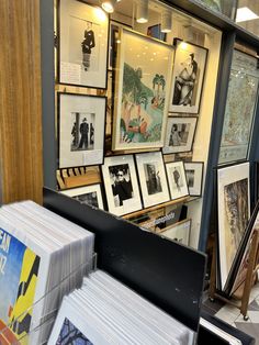 many framed pictures are on display in front of a store window with books and magazines