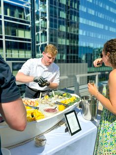 a man and woman standing in front of a buffet on top of a building with food