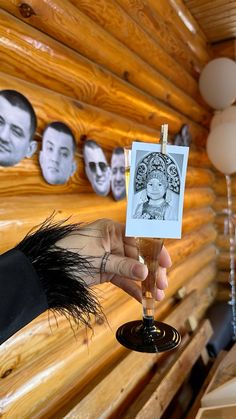 a person holding a wine glass in front of a wooden wall with pictures on it