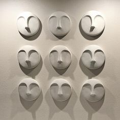 nine masks are arranged in the shape of faces on a white wall, each with different shapes and sizes