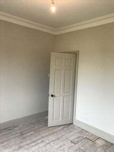 an empty room with white walls and wood flooring in the foreground is a door to another room