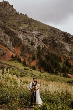 a bride and groom standing in front of a mountain