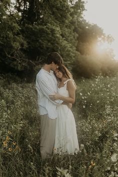 a man and woman standing in tall grass with the sun shining through trees behind them