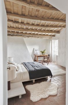 a bed sitting under a wooden ceiling next to a table and chair in a room