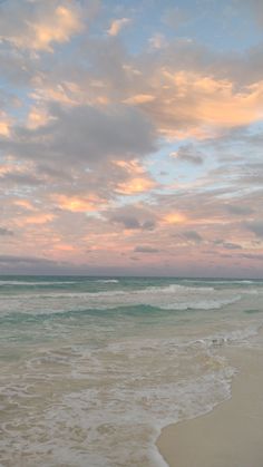 an ocean beach with waves coming in to shore and the sun setting on the horizon