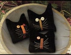 three black cat pillows sitting on top of a wooden bowl filled with flowers and plants