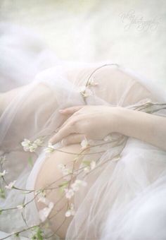 a woman in white dress laying down with her hands on her chest and flowers growing out of her stomach