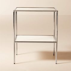 a glass and metal side table with one shelf on the bottom, against a beige background