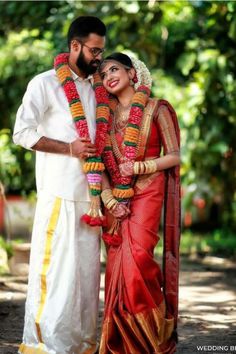 a man and woman standing next to each other in front of trees with garlands around their necks