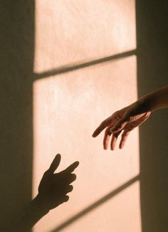 two hands reaching out towards each other in front of a window with light coming through