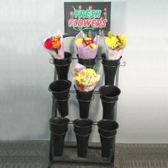 a bunch of flowers that are in some black vases on a stand with a sign behind them