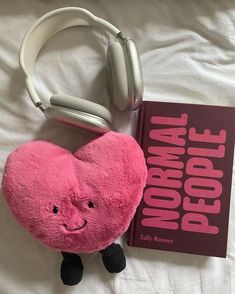 a pink stuffed animal with headphones next to a book on a white bed sheet