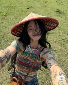 a woman with tattoos and a straw hat on her head holding a purse in the grass