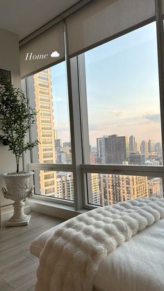 a bed sitting next to a large window in a room with high rise buildings behind it