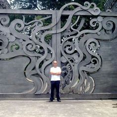 a man standing in front of a metal gate with an intricate design on the side