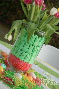 a vase filled with candy and flowers sitting on top of a white table covered in green grass