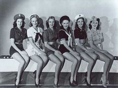 six women in sailor uniforms are posing for a photo on a stage with their legs crossed