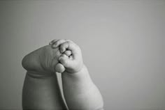 a black and white photo of a baby's hand holding the top of its foot