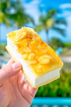 a person holding up a piece of food in front of the ocean and palm trees