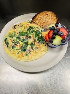 a white plate topped with an omelet next to a bowl of fruit and toast