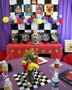 a purple table topped with lots of balloons next to a checkerboard wall covered in pictures