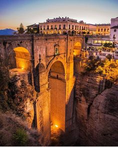 an old stone bridge over a river with buildings in the background at night, and lit up by street lights