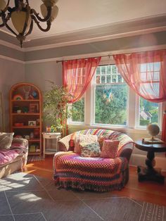 a living room filled with furniture and a large window covered in red drapes on the windowsill