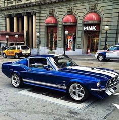 a blue and white mustang parked in front of a pink store on a city street