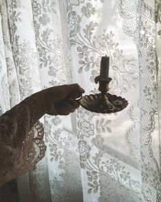 a person is holding a candle in front of a window with white lace on it