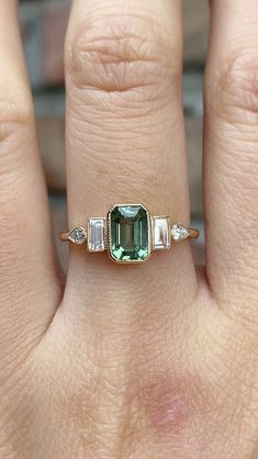 a woman's hand with a ring on it and an emerald stone in the middle