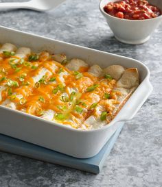 a casserole dish with chicken, cheese and green onions in it next to a bowl of salsa