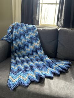 a blue and white crocheted blanket sitting on top of a couch next to a window