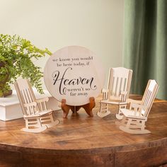 a wooden table topped with rocking chairs next to a potted plant and a plaque