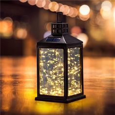 a small lantern is lit up with fairy lights on it's sides and sits on a table