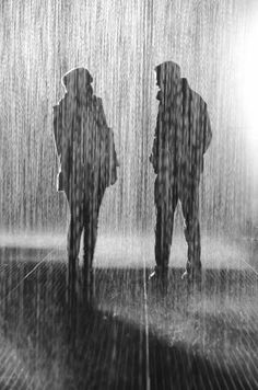 two people standing in the rain with their backs to each other, one is holding an umbrella