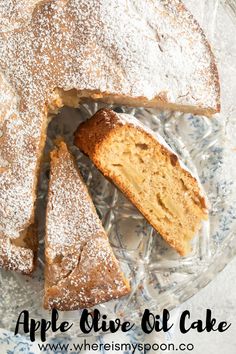 an apple olive oil cake with powdered sugar on top is cut into slices and sits on a glass platter