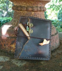 a leather journal with a pen and paper clip attached to it sitting on a stone pedestal