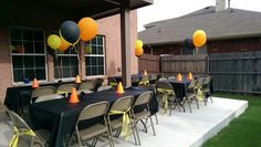 an outdoor party with black table cloths and orange and yellow balloons on the tables