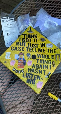 a yellow graduation cap sitting on top of a metal table next to plastic bags and pens