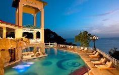 an outdoor swimming pool with lounge chairs around it and the ocean in the back ground