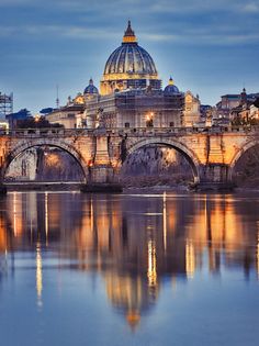 a bridge that is over some water with a building in the background and lights on