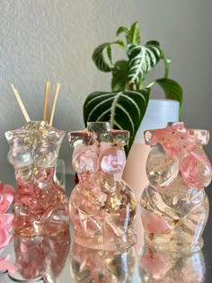 three glass bears sitting on top of a table next to a potted plant and candle holder