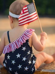 a baby sitting on the ground with an american flag in her lap and wearing a swimsuit