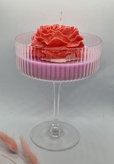 a pink cake in a glass dish on a white tablecloth with feathers around it