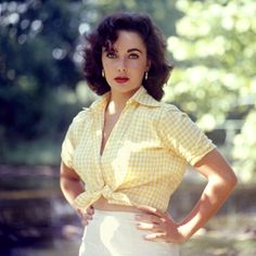 a woman standing with her hands on her hips wearing a yellow shirt and white skirt