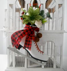 a white shoe with a red and black plaid ribbon tied around it sitting on top of a birdcage